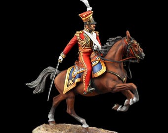May include: A detailed figurine of a soldier on horseback. The soldier wears a red uniform with gold accents, a tall hat, and a white sash. The horse is brown with a black mane and tail, and the base is a light tan color.
