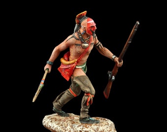 May include: A painted figurine of a Native American warrior wearing a red and white feathered headdress, holding a rifle and a tomahawk. The warrior is painted with red and black face paint and has a beaded necklace.