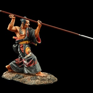 May include: A hand-painted figurine of a samurai warrior in a black and red robe, holding a spear in a fighting pose. The figurine is standing on a small, rocky base.