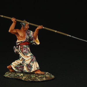 May include: A hand-painted figurine of a Japanese warrior in a colorful robe, holding a spear in a fighting stance. The figurine is standing on a small, rocky base.