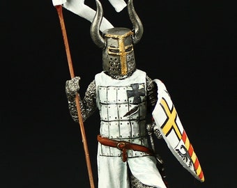 May include: A hand-painted miniature figure of a knight in white armor with a black cross on his chest. He is holding a spear and a shield with a yellow cross and a red and yellow eagle. The knight is wearing a helmet with horns and a white cape.