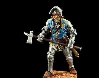 Puede incluir: Una figurita de metal pintada a mano de un soldado medieval con armadura y sosteniendo un hacha de batalla. El soldado lleva una túnica azul y amarilla y un casco con visera. La figurita está de pie sobre una base marrón.