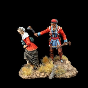 May include: A painted miniature figure of a man in a red coat and blue sash holding a club, chasing a woman in a red and green dress. The figures are standing on a brown base with green and brown grass.