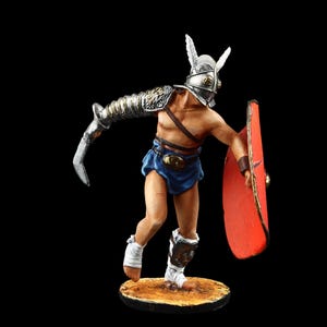 Peut inclure: Une figurine peinte d'un gladiateur portant un casque argenté avec une crête de plumes rouges et blanches, un pagne bleu et un bouclier rouge. Le gladiateur tient une épée dans sa main droite et est en position de combat.