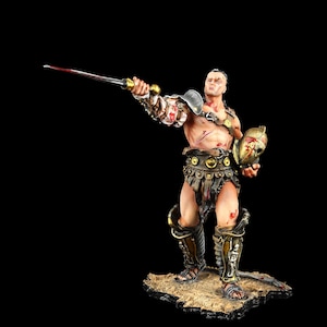 May include: A detailed figurine of a gladiator, holding a bloodied sword and a helmet. The figure is clad in armor and leather, with visible wounds. The base is a textured, sandy surface, set against a black background.