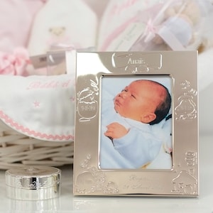 Op de afbeelding: Zilveren fotolijst met een babyfoto erin. De lijst heeft een decoratief ontwerp met een baby in een mandje en de tekst "Anais" en "Gedoopt op 21 april 2014".