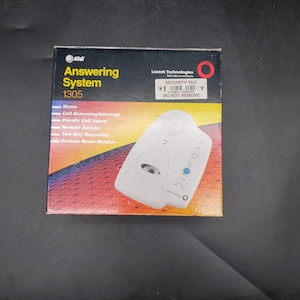 Könnte beinhalten: Ein AT&T Answering System 1305 mit Funktionen wie Memo und Fernzugriff wird auf der Originalverpackung gezeigt. Die Box hat ein farbenfrohes Design mit dem Lucent Technologies Logo und einem Sicherheitsetikett.