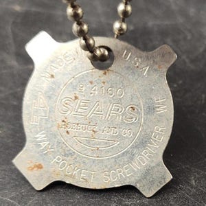 May include: A vintage, silver-coloured Sears 4-way pocket screwdriver on a ball chain. The tool is stamped with the text "MADE IN U.S.A." and "SEARS ROEBUCK AND CO."