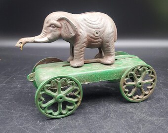 Carro de juguete antiguo de hierro fundido con forma de elefante y mecanismo de ruedas, color verde.