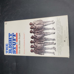 Puede incluir: Una cinta VHS de la película "Elegidos para la gloria" con astronautas con trajes espaciales. El título es azul y rojo, con la frase "How the future began". Es un lanzamiento de Warner Bros.