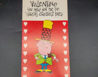 May include: Valentine's Day card with a cartoon illustration. The card features a man in a tall hat decorated with hearts. The text reads "Valentine, You May Not Be The World's Greatest Lover."