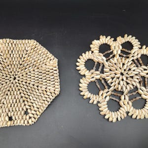 Puede incluir: Dos posavasos decorativos. Uno tiene forma de octágono y el otro de flor. Ambos están hechos de pequeñas piezas ovaladas de color claro, posiblemente conchas o cuentas, dispuestas en un patrón.