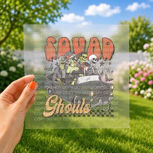 May include: A clear transfer sheet featuring a graphic of a vintage car carrying a group of skeletons and a witch. The text reads SQUAD Ghouls in a retro font. The design includes small bats and stars, set against a checkered pattern base.