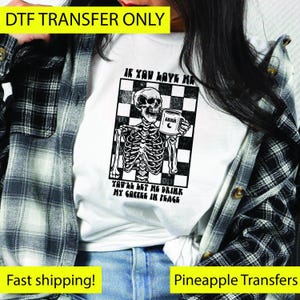 May include: White t-shirt with a black and white graphic of a skeleton holding a coffee mug. The graphic is set against a checkered background and includes the text "IF YOU LOVE ME, YOU'LL LET ME DRINK MY COFFEE IN PEACE."