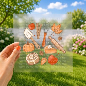 May include: A square frosted transfer sheet featuring a colorful autumn-themed illustration of a red apple, cinnamon sticks, a wire whisk, a maple leaf, a pumpkin, a rolling pin, a slice of pumpkin pie, a cinnamon roll, and an acorn.
