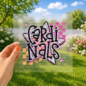 May include: A clear transfer sheet featuring a large, five-pointed star with a black and white polka dot pattern. The word CARDINALS is printed in bold, black, outlined letters across the star, set against a background of orange and pink checkered squares.