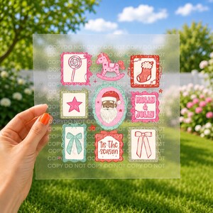 May include: A clear sheet featuring a grid of nine festive illustrations including a lollipop, a rocking horse, a Christmas stocking, a pink star, a Santa Claus figure, text reading HOLLY & JOLLY, a bow, text reading tis the season, and a ribbon.