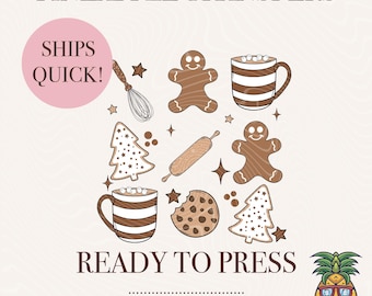 May include: A set of 10 ready-to-press iron-on transfers featuring a winter holiday theme. The designs include gingerbread people, hot chocolate mugs, Christmas trees, and a rolling pin. The transfers are cold peel and come with a pineapple graphic.