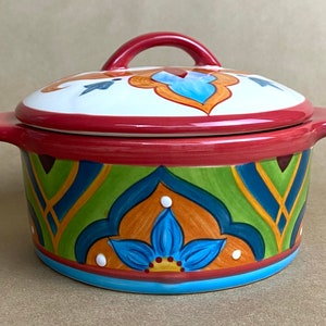 May include: A colorful ceramic casserole dish with a lid. The dish has a red rim and a blue, green, orange, and yellow geometric pattern. The lid has a red handle and a white center with a blue and orange design.