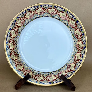 May include: A white porcelain dinner plate with a gold, red, blue, and green floral border design.