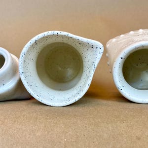 May include: Three white ceramic jugs with speckled and textured surfaces. The jugs are empty and ready to be filled.