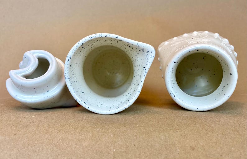 May include: Three white ceramic jugs with speckled and textured surfaces. The jugs are empty and ready to be filled.