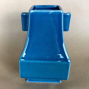 May include: A blue ceramic vase with a square top and two handles. The vase has a crackled glaze finish.