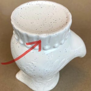 May include: White ceramic hand-shaped vase with a speckled glaze and a beaded rim. The vase has a floral design.