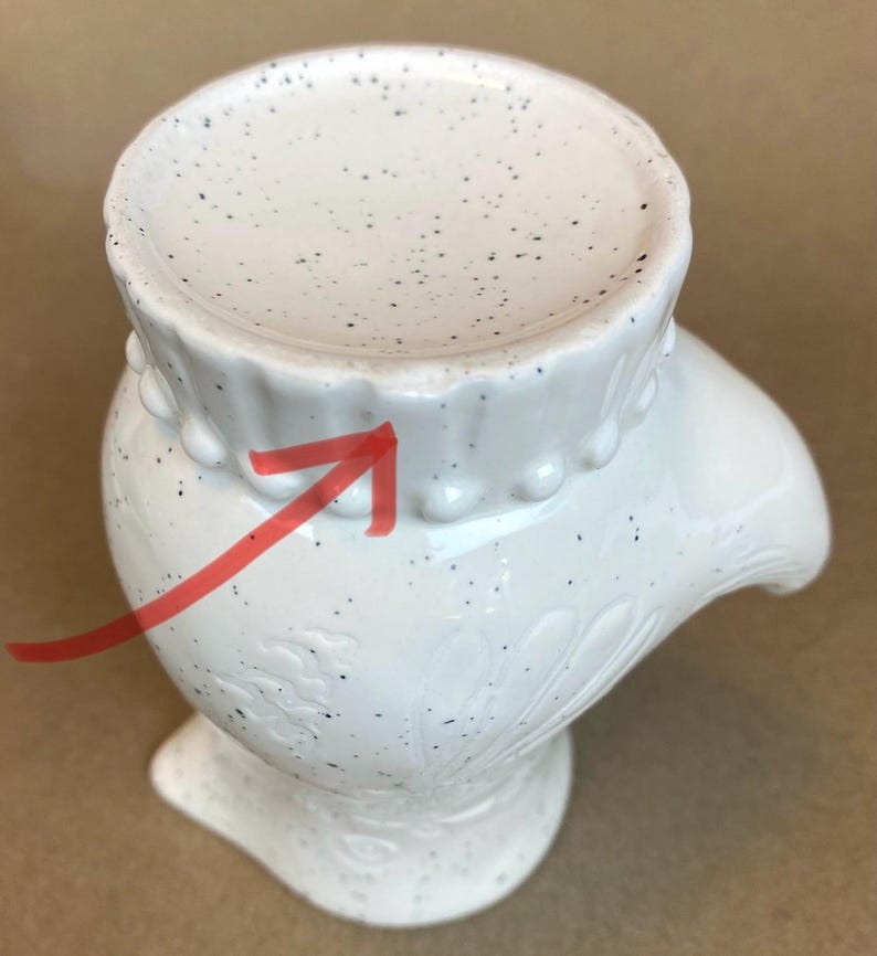May include: White ceramic hand-shaped vase with a speckled glaze and a beaded rim. The vase has a floral design.