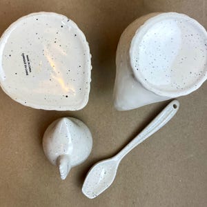 May include: White ceramic chicken-shaped sugar bowl and creamer set with a speckled finish. The set includes a small spoon. The bottom of the sugar bowl reads "Made in China, Fabriqu&eacute; en Chine".