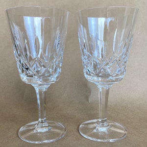 May include: Two clear glass wine glasses with a cut crystal design. The glasses have a tall, slender stem and a round base.