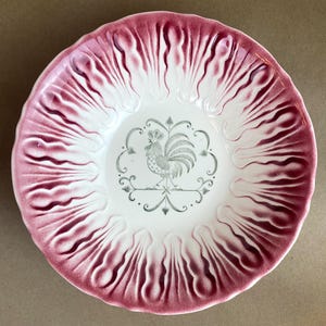 May include: A white ceramic bowl with a pink and white swirl design. The bowl features a green rooster design in the center.