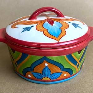 May include: A colorful ceramic casserole dish with a lid. The dish has a red rim and a blue, green, orange, and yellow floral pattern. The lid has a red handle and a similar floral pattern.