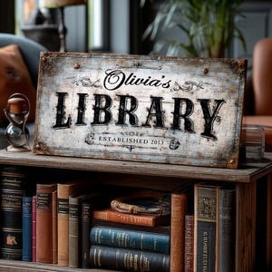 May include: A rustic wooden sign that reads "Olivia's LIBRARY ESTABLISHED 2013" sits atop a wooden bookshelf filled with antique books. The sign has a distressed, vintage look with dark lettering and decorative flourishes. The bookshelf is made of dark wood.