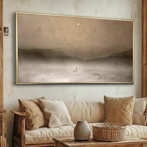 May include: A framed landscape painting with a muted color palette. The artwork depicts a serene scene with mountains, a figure, and a moon. The frame is gold, and the overall aesthetic is minimalist and calming.