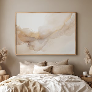 May include: A framed abstract art piece with a neutral color palette of beige, cream, and gold tones. The artwork features flowing, watercolor-like shapes with gold accents. The piece is displayed above a bed with neutral-colored bedding.