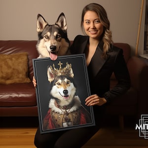 May include: A woman holds a framed portrait of a dog wearing a gold crown and a red and gold robe. The dog is looking directly at the camera with a happy expression. The portrait is set against a dark background.