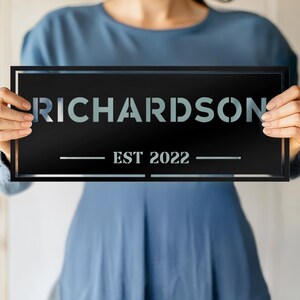 May include: Black rectangular sign with white text that reads "RICHARDSON EST 2022".