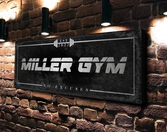 May include: Black sign with white text that reads "MILLER GYM" with the words "EST 2022" and "NO EXCUSES" above and below the gym name. The sign is mounted on a brick wall.