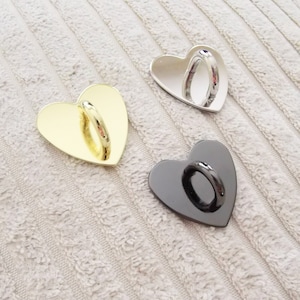 May include: Three heart-shaped phone ring holders in gold, silver, and black.