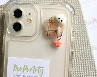 May include: A clear phone case with a white and pink charm attached. The charm is a small cloud with a plaid pattern and a pink star hanging from it. The phone case has a sticker on it that says "Mo Po Artz by Amy Trieu - Etsy UK".