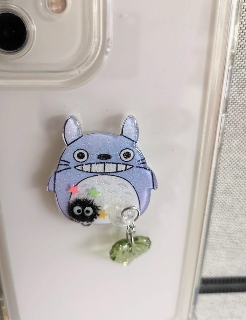 May include: A blue and white Totoro character phone charm with a small black soot sprite character and green leaves.
