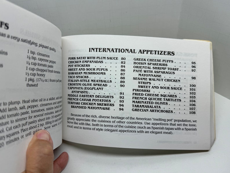 May include: A page from a cookbook featuring a list of international appetizers with their corresponding page numbers. The appetizers include Pork Satay with Plum Sauce, Chicken Empanadas, Pot Stickers, Sweet and Sour Pupus, Hawaiian Mushrooms, Taco Snacks, Italian-Style Meatballs, Crostini Olive Spread, Caponata (Eggplant Antipasti), Middle Eastern Delights, French Caviar Potatoes, Teriyaki Chicken Skewers, and Brandied Mayonnaise.