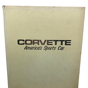 Puede incluir: Libro Corvette vintage de color crema con las palabras "CORVETTE America's Sports Car" impresas en negro. El libro tiene una superficie texturizada y muestra signos de desgaste.