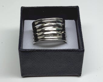 May include: A silver-toned ring with a multi-band design, presented in a black jewelry box with a white interior. The ring features multiple horizontal bands, creating a layered effect. The box has a textured exterior.