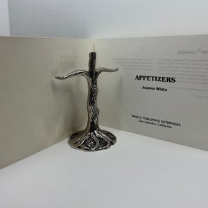 May include: A silver metal tree-shaped stand for holding napkins or other small items. The stand is on a white surface with a book titled "Appetizers" by Joanna White. The book is published by Bristol Publishing Enterprises in San Leandro, California.