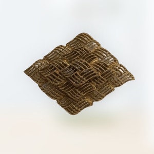 Könnte beinhalten: Eine goldfarbene, gewebte Brosche in Diamantform. Die Brosche besteht aus einem filigranen, komplizierten Design aus miteinander verwobenen Metallfäden.