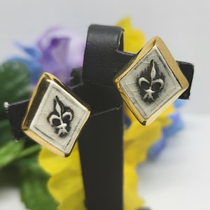 May include: A pair of gold earrings with a white and black enamel fleur-de-lis design.