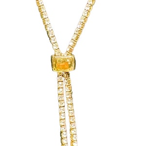 May include: A gold chain necklace with a small square-shaped pendant. The chain is made of small, round beads.