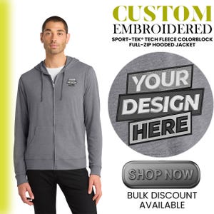 May include: A man wearing a gray Sport-Tek Tech Fleece colorblock full-zip hooded jacket. The jacket has a custom embroidered design and the text "YOUR DESIGN HERE". The image also includes the text "SHOP NOW" and "BULK DISCOUNT AVAILABLE".